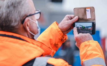 Mann in orangener Baustellenjacke fotografiert mit Handy